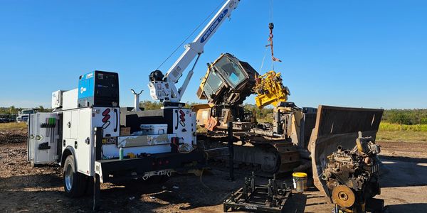 Heavy machinery and a service truck working on an excavator engine outdoors.