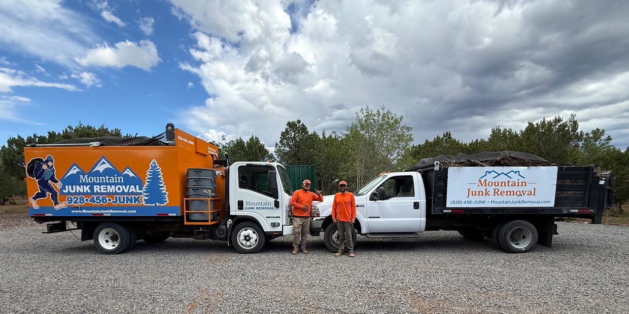 Two junk removal trucks facing each other, two crew members smiling, with cloudy skies