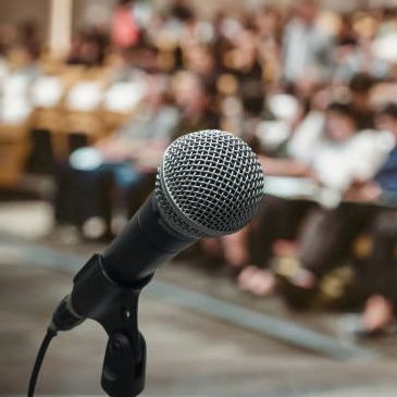 Close-up of a microphone on stage with a blurred audience in the background.