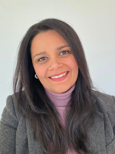 Smiling woman with long dark hair in a gray blazer and pink turtleneck.