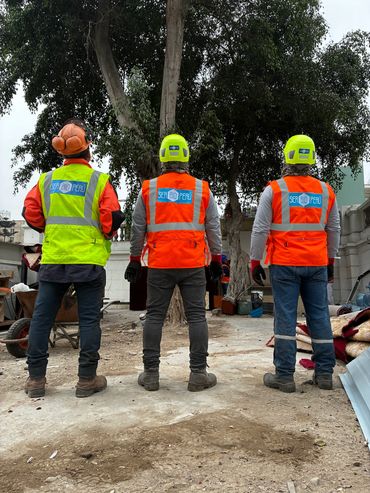 Three construction workers in safety gear standing with backs to the camera.