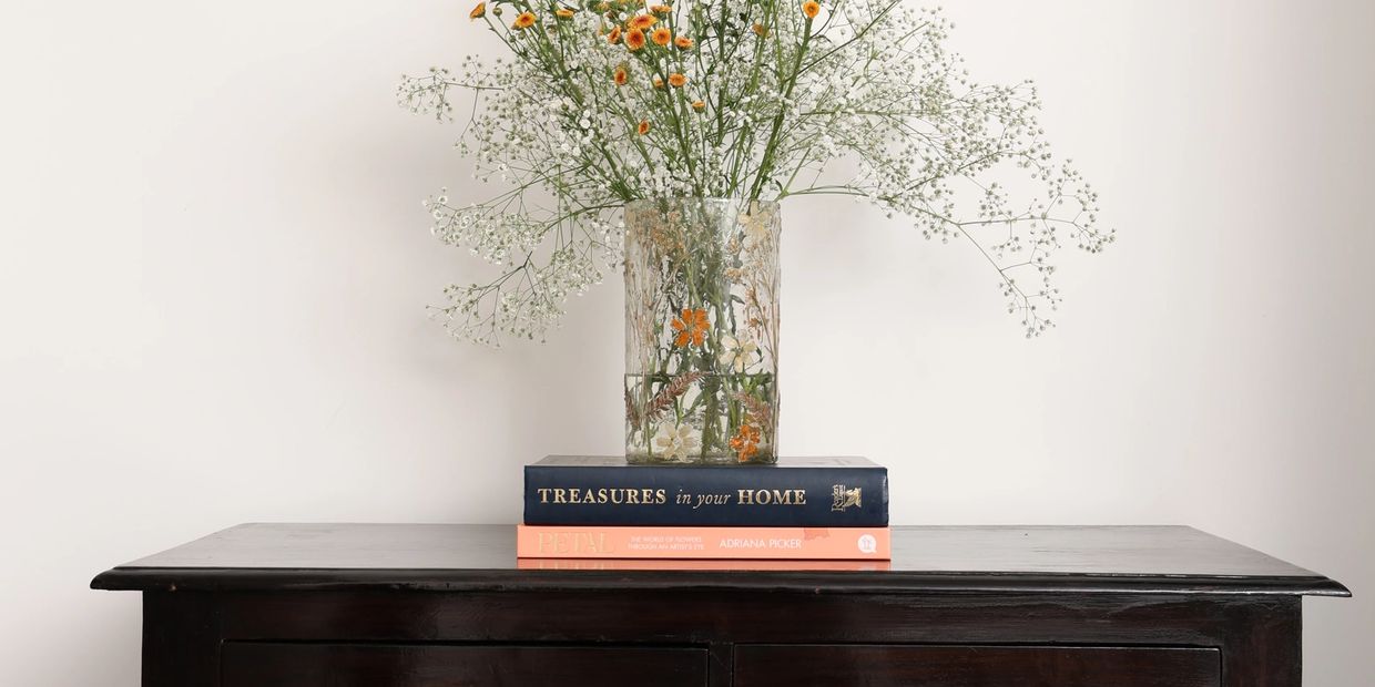 A dark wooden dresser with a vase of flowers and two books on top.