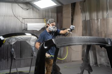 Worker spray painting a car part in a workshop.