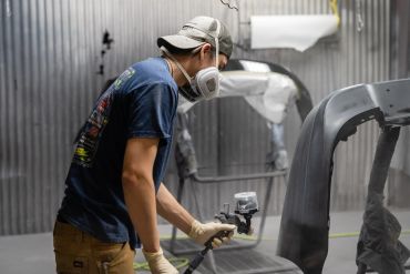 Man spray painting a car part in a workshop.
