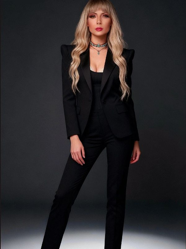 Woman in a sleek black suit and high heels, posing confidently against a dark background.