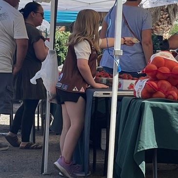 People shopping at an outdoor farmers market with fresh produce and tents.