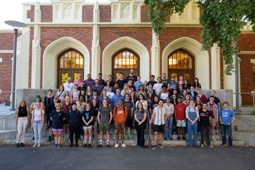 Large group posing in front of a historic brick building with arched windows.