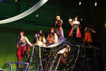 Actors in pirate costumes performing on a dark stage with nets and ropes.