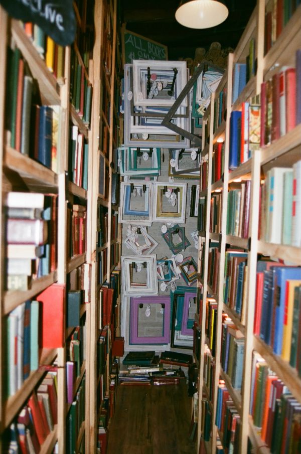Narrow aisle between tall bookshelves with empty picture frames on the back wall.