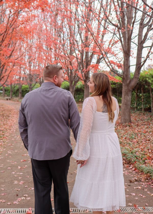 Couple holding hands walking under autumn trees.