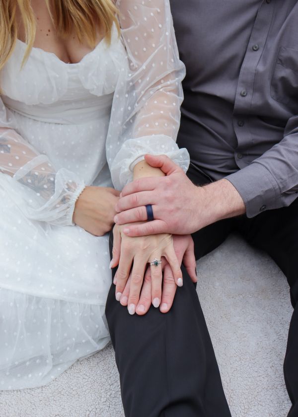 Couple holding hands with engagement rings visible.