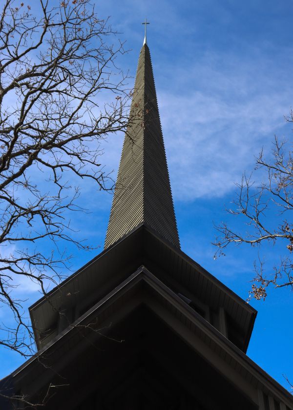 Tall church steeple with a cross on top against a blue sky.