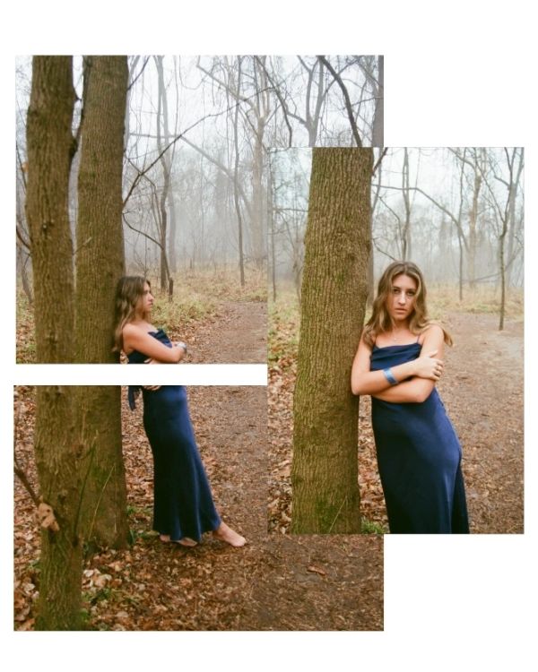 Woman in blue dress leaning against a tree in the woods.