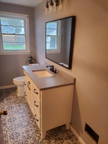 Bathroom remodel with new flooring, vanity, concrete looking countertop, paint, and shower surround