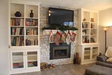Custom mantel hung with Christmas stockings and built-ins featuring glass paneled base cabinet doors