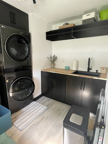 Carbon black stained maple cabinetry with stacked washer/dryer and hanging pole space above the sink