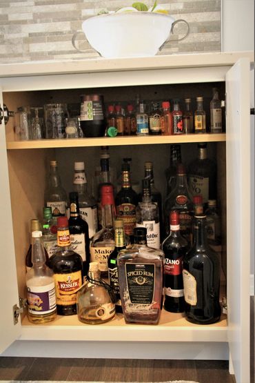 Tiered booze bottle storage in base cabinet with adjustable shelf above