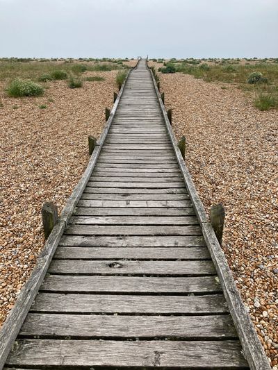 Long wooden boardwalk stretches over a rocky beach towards the horizon.