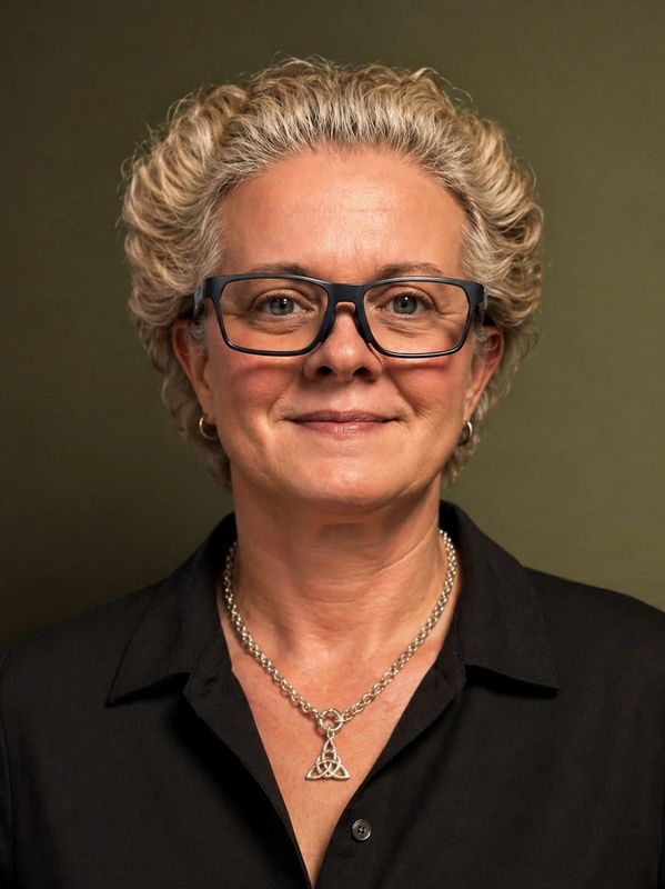 Smiling woman with curly hair, glasses, and a silver necklace.