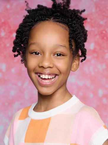 Smiling child with curly hair against a pink background.