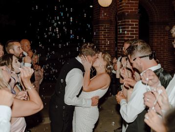 Bride and Groom kissing during their formal exit surrounded by guests blowing bubbles