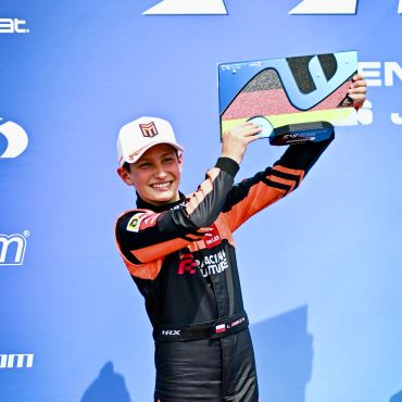 Młody kierowca wyścigowy trzymający trofeum na podium.