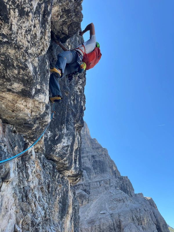 Two climbers ascending a steep rocky mountain under a clear blue sky.