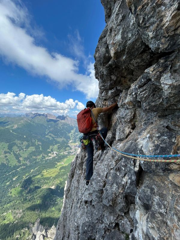 A climber ascends a steep rock face with a scenic valley below.