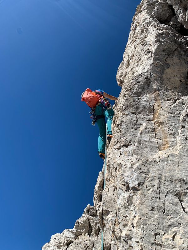 A climber ascends a steep rock face under a clear blue sky.