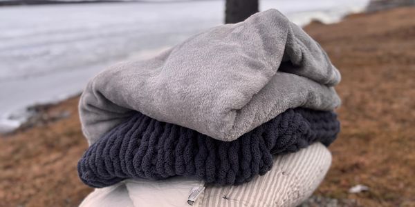 Folded cozy blankets stacked outdoors near a water body.