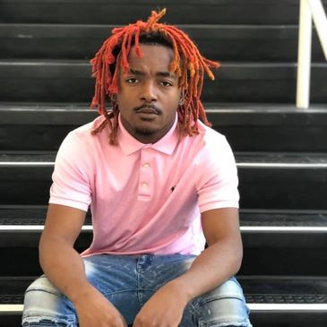 Young man with red dreadlocks wearing a pink polo shirt sitting on stairs.