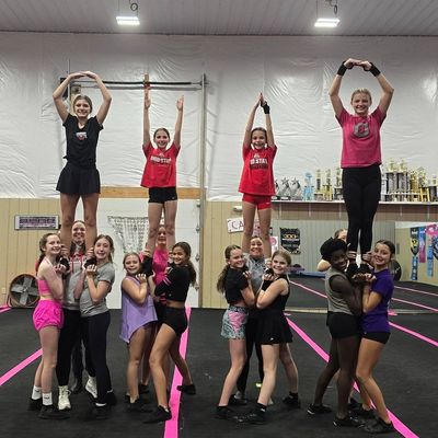 Cheerleading group performing stunt with four flyers held up.