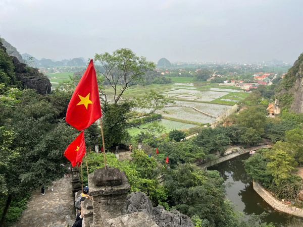Vietnamese flags along a stone path overlooking lush green fields and a river.