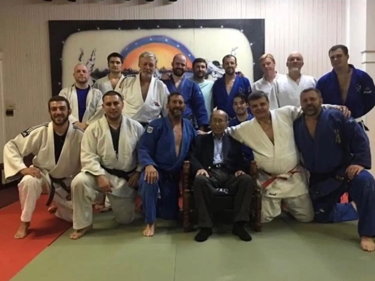 Group photo of martial artists in judo gis with an elderly man seated in the center.
