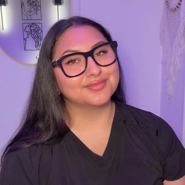 Young woman with glasses smiling against a purple-lit background.