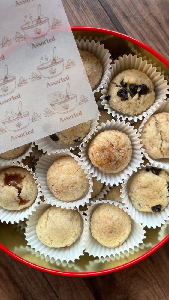 Assorted homemade cookies in paper cups inside a red tin.