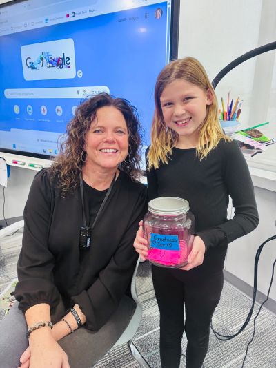 Woman and girl smiling, holding a jar labeled "Greatness jar."