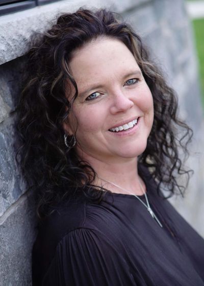 Woman with curly hair smiling against a stone wall.