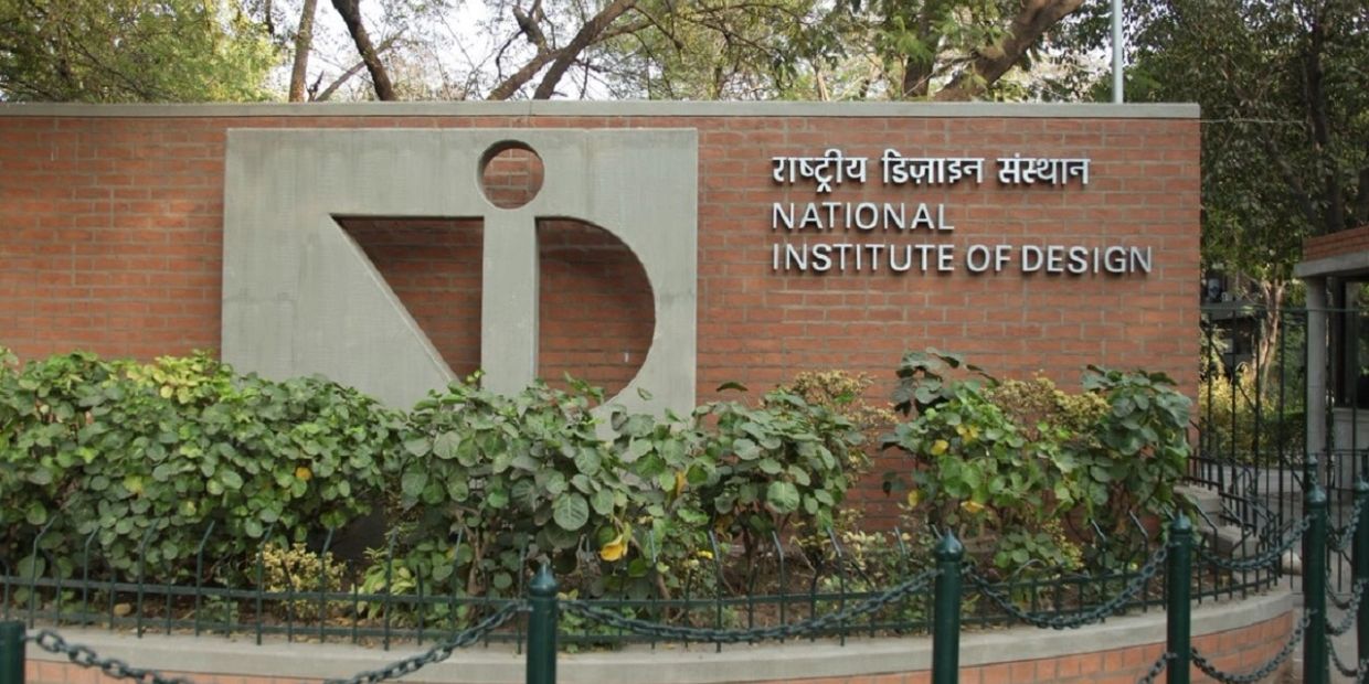 Entrance sign of the National Institute of Design with greenery and brick wall.
