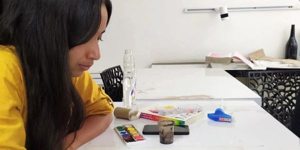 A woman in yellow painting a realistic portrait on paper.
