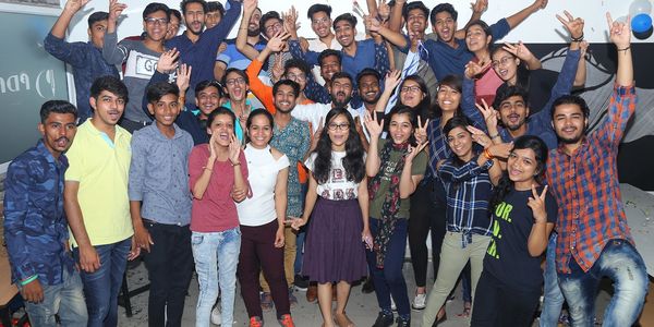 A large group of young people celebrating indoors, making joyful hand gestures and smiling.
