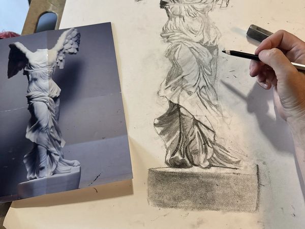 A close-up of a person drawing the Winged Victory of Samothrace statue.