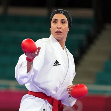 Female karate athlete in a white gi with red gloves and belt.