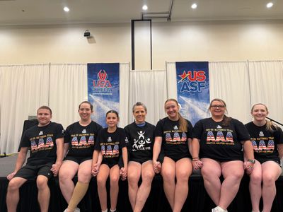 Pictured, 7 cheerleaders and coaches from ParaCheer Spirit sitting on a stage where they presented P