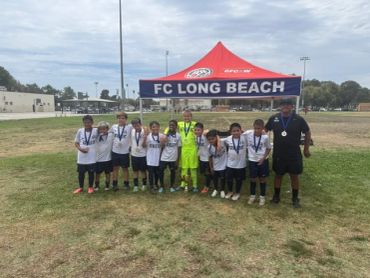 Youth soccer team posing under FC Long Beach tent.