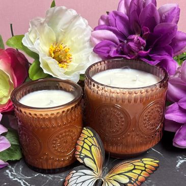 Decorative candles with floral and butterfly accents on a marble surface.