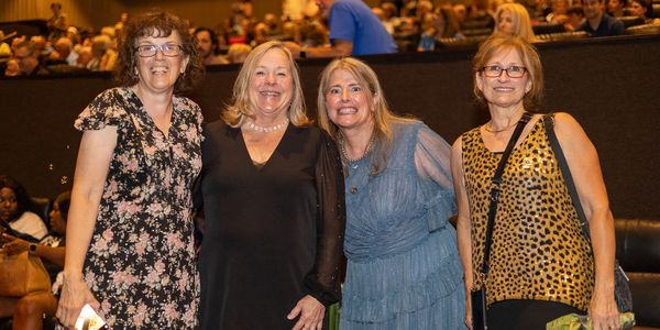 A group of women stand huddled together smiling at an event.