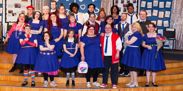A diverse group in blue dresses and costumes posing on stage steps.