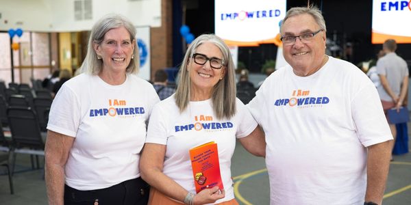 Three smiling adults wearing "I Am Empowered" shirts at an indoor event.