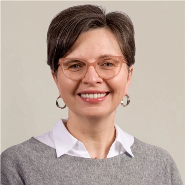 Woman smiling, wearing glasses and hoop earrings.